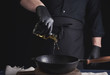 chef in black latex gloves pours olive oil from a transparent bottle into a black cast-iron frying pan