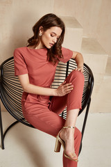 Wall Mural - Beautiful sexy brunette woman tanned skin face cosmetic makeup wear pink suit pants for date walk office fashion clothes style collection interior room  sand color safari summer armchair palm boho.