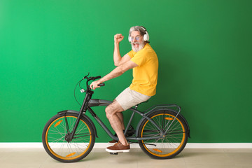 Wall Mural - Happy elderly man with bicycle and headphones near color wall