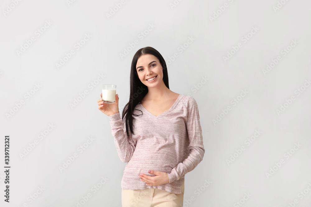 Beautiful pregnant woman with milk on light background