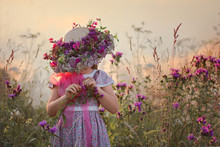 Adorable Little Girl In A Handmade Hat Decorated With Fresh Wildflowers.