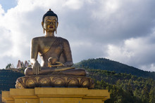Low Angle View Of Golden Buddha Statue By Tree Mountain Against Cloudy Sky