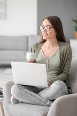 Canvas Print - Beautiful young woman working on laptop and drinking coffee at home