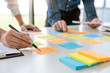 © snowing12 - Business people arranging sticky notes commenting and brainstorming on work priorities colleague in a modern co-working space.