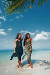 two beautiful twin sisters in elegant dresses having fun on tropical beach