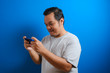 © Reza - photo of a fat Asian man wearing a gray T-shirt looking happy playing a game on his smartphone