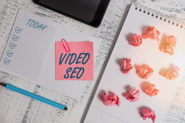 Poster - Handwriting text Video Seo. Conceptual photo the process of improving the ranking or visibility of a video Squared spiral notebook marker smartphone paper balls note clip wooden