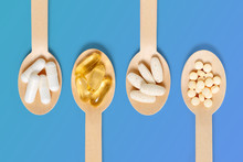 Vitamin supplements on wooden spoon against blue background