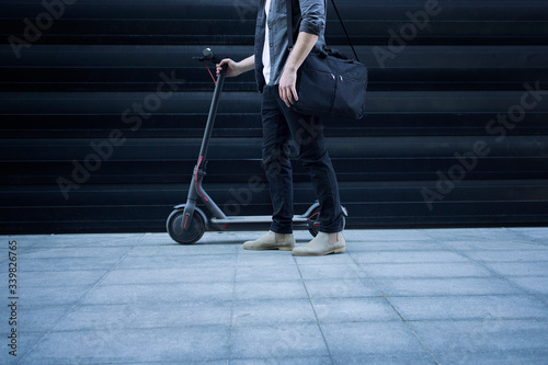 Shot of an unrecognizable handsome person with shoulder bag standing by his electric scooter. Best city commuting vehicle.