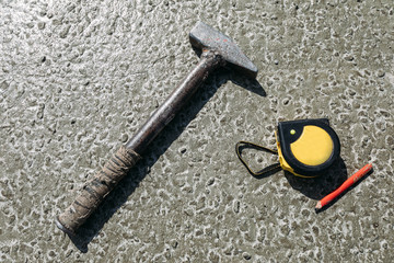 old hammer, tape measure and red pencil on a concrete floor