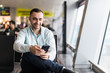 © F8  \ Suport Ukraine - TPortrait of handsome man in casual wear holding his luggage and messaging through his mobile phone while sitting in the hall of the airport