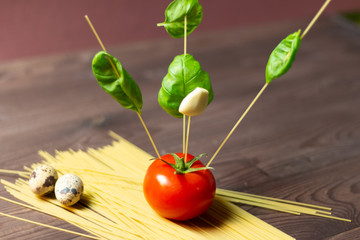 Wall Mural - Installation of Tomato with stick spaghetti with green basil leaves and garlic on pasta bunch with quail eggs on brown background