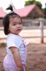 A cute Asian girl standing outdoor, close to a barn, turning her head as her mother calls.