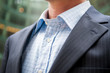 Close-up of unrecognizable businessman in dark pinstripe suit and unbuttoned shirt collar standing outdoors in an office building courtyard