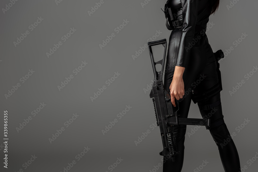 cropped view of futuristic african american woman posing with assault rifle on grey - obrazy, fototapety, plakaty 