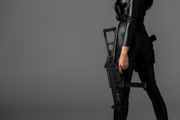 Wall Mural - cropped view of futuristic african american woman posing with assault rifle on grey