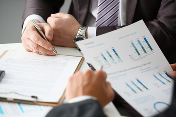 Male arm in suit and tie fill form clipped pad with silver pen closeup. Sign gesture read pact sale agent bank job make note loan credit mortgage investment finance executive chief legal teamwork law