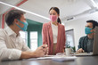© AnnaStills - Young businesswoman in protective mask talking to her colleagues during business meeting at office