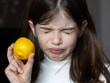 Small / young girl tastes a lemon, grimace on her face