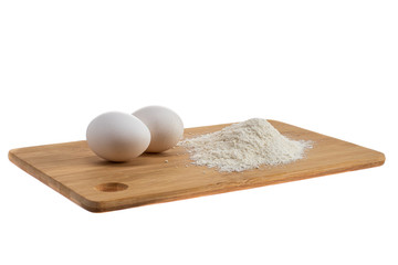 two white eggs on a wooden board and next to a handful of flour