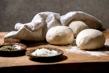 Wall Mural - Dough for italian pizza napolitana cooking. Three balls of fresh homemade wheat dough and ingredients in ceramic plates above on wooden kitchen table. Home baking.