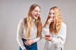 © Przemek Klos - Young women girls listening to music together streaming content having fun watching video enjoying video chat talking with friends making gestures faces using smartphone earphones headphones