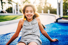 Portrait Of Smiling Tween Girl Sitting In Park At Sunset