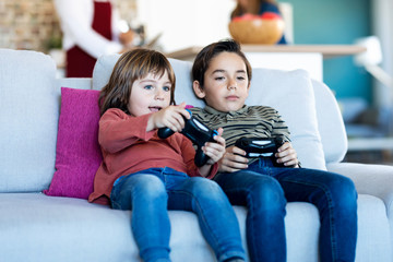 Wall Mural - Two nice brothers playing video games while sitting on the sofa at home.