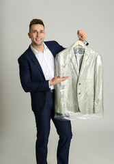 Poster - Man holding hanger with jacket in plastic bag on light grey background. Dry-cleaning service