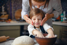 Young Woman In Formal Clothing Having Fun While Making Dough With Little Adorable Girl In Modern Kitchen.