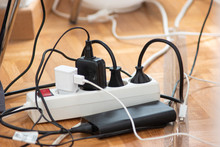 Messy Outlet Power Extension Cord On An Apartment Floor With Various Charging Devices Plugged In