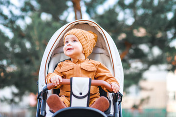 A cute little beautiful one year old boy is sitting and smiling in a stroller