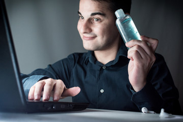 Hombre joven trabajando en casa mostrando un sanitizante Hombre sosteniendo sanitizer. hombre de negocios contento trabajando en su casa. Covid-19. Young man with laptop