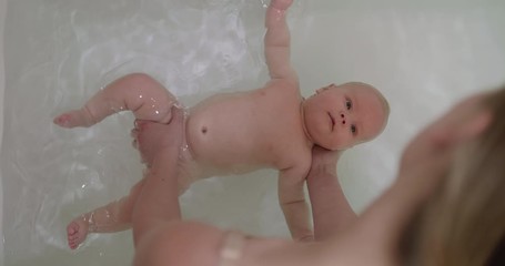 top view of funny newborn baby swimming during bathing with mother's help