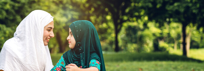 Wall Mural - Portrait of happy religious enjoy happy love asian family arabic muslim mother and little muslim girls child with hijab dress smiling and having fun moments good time in summer park