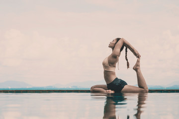 Wall Mural - Vacation of Attractive Asian woman relaxing in yoga king pigeon pose on the pool above the beach with beautiful sea in Tropical island,Feeling comfortable and relax in holiday,Vacations Concept