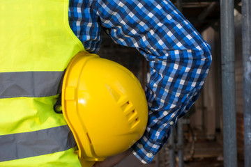 Cropped image of a construction worker wearing a yellow safety vest and keeping a yellow helmet underarm