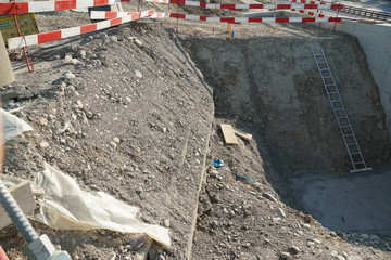 Construction pit or shaft on a civil engineering construction site with a metal ladder for better access surrounded by barrier planks in red and white.