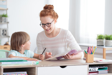 Wall Mural - Happy mother and smiling son doing homework at desk