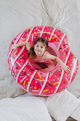 Wall Mural - Summer vacation on quarantine, a kid with donut tube at home, baby girl with pink rubber ring, home self-isolation in summer