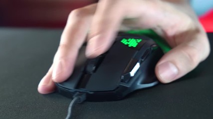 A gamer is playing in a computer club. In the frame, the hand of a gamer and a gaming mouse. Red and violet colors. ESports competitions.



