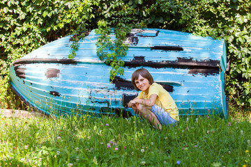 A boy is sitting at a wooden boat in summer yard