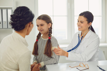 Wall Mural - A woman pediatrician makes a setoscope examination to a child girl with mom in a clinic office.