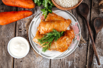 Wall Mural - Top view on a dish of eastern european cuisine golubtsy stuffed cabbage leaves with meat, with sour cream and carrot, horizontal