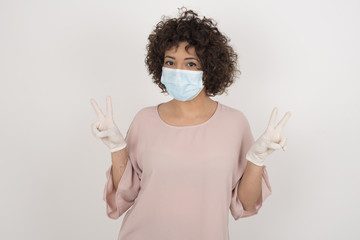 Wall Mural - Indoor portrait of young caucasian female isolated on gray background with optimistic smile, showing peace or victory gesture with both hands, looking friendly. V sign.