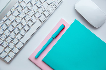 colorful notebooks, pen, computer keyboard and mouse on a white table