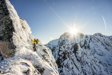 Wall Mural - An alpinist climbing a steep ice, snow and rock face in alpine like mountain landscape of High Tatras, Slovakia. Winter extreme mountaineering and alpinism on alpine peaks. Sunset over a climber.