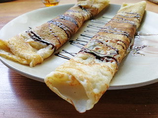 pancakes rolled into a tube lying on a plate and poured with chocolate on top.