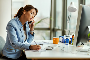 Wall Mural - Businesswoman taking notes while making a phone call in the office.