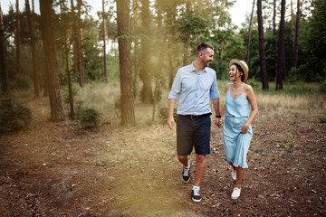 Cheerful couple in love spends time together, they walk through the woods on a summer evening